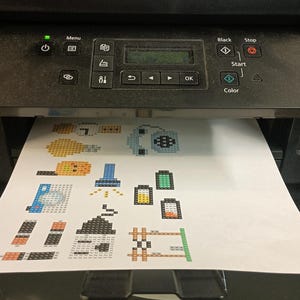 May include: A white sheet of paper with colorful pixel art designs printed on it. The designs include a light blue robot, a yellow light bulb, a blue toolbox, a green battery, a yellow battery, a brown fence, and a gray and white lamp.