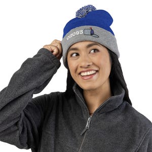 May include: A blue and gray knit beanie with a pom-pom on top. The hat features the embroidered text "02093" and a mailbox graphic. The person in the image is wearing a gray fleece jacket.
