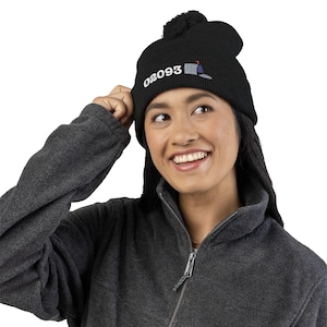 May include: Black knit beanie with a pom-pom on top. The beanie features the number "02093" in white, along with a small mailbox graphic. The person in the image is wearing a dark gray fleece jacket.