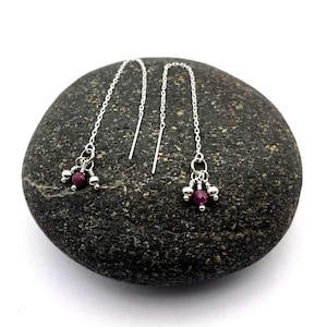 May include: A pair of silver dangle earrings with a cluster of small, round, purple gemstones hanging from each chain.