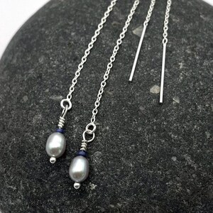 May include: A pair of silver dangle earrings with a pearl and a blue gemstone on each earring. The earrings are hanging from a silver chain.