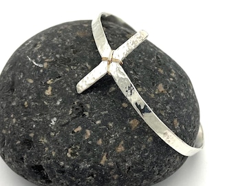 May include: A silver hammered bangle bracelet with a silver cross charm. The cross is attached to the bracelet with a thin gold wire.