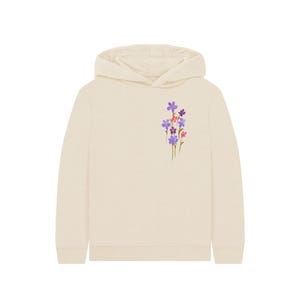 May include: A cream-colored hoodie with a floral design on the left chest. The flowers are purple, pink, and red. The hoodie has a hood and long sleeves. A casual, comfortable garment.
