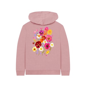 May include: A dusty rose hoodie featuring a vibrant floral design on the back. The colorful bouquet includes pansies, daisies, and other wildflowers in shades of pink, yellow, red, and purple. The hoodie has a hood and long sleeves.
