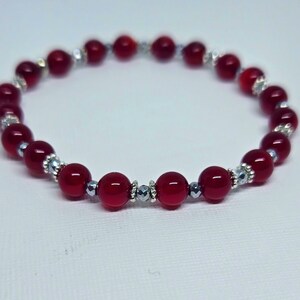 May include: A red beaded bracelet with silver accents. The bracelet features round, glossy red beads interspersed with silver-colored decorative elements. The beads are strung together on an elastic band, creating a flexible and stylish accessory.