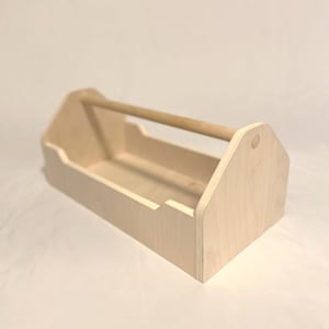 May include: A light-colored wooden tool box with a natural wood handle. The box is rectangular with angled sides and a low front. The handle is a rounded dowel. The tool box is empty.