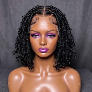 May include: A shoulder-length black wig featuring textured, coiled locs with a defined center part. The wig is displayed on a smooth, tan-colored mannequin head with a lace front hairline that shows natural-looking edges and baby hairs.