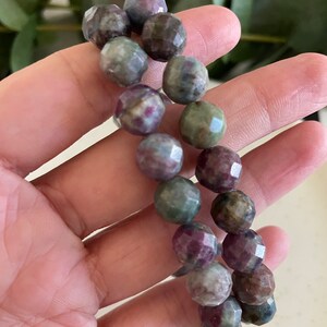 May include: A bracelet made of faceted, multi-colored gemstone beads. The beads are a mix of green, pink, and brown.