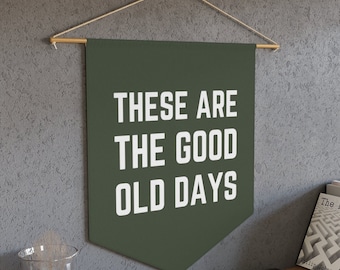 May include: A green canvas banner with the text "These are the good old days" in white lettering. The banner is hanging from a wooden dowel rod with string.