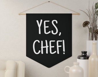 May include: Black banner with white text that reads "YES, CHEF!" hanging on a white wall.