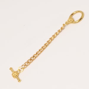 May include: A gold-colored tie chain with a T-bar clasp and a loop at the other end. The chain is composed of a curb chain and a twisted chain section. The T-bar clasp and loop feature floral detailing.