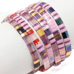 Peut inclure: Collection de six bracelets en carrelage rose. Chaque bracelet est composé de petits carreaux rectangulaires roses, avec des accents dorés et irisés. Les bracelets sont disposés en ligne incurvée, mettant en valeur leur design.