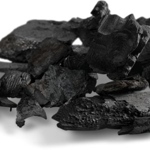 May include: A close-up of a pile of black charcoal briquettes. The briquettes are irregularly shaped and have a rough, textured surface.