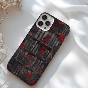 May include: A black phone case with a pattern of red roses and old books. The case has a camera lens cutout.