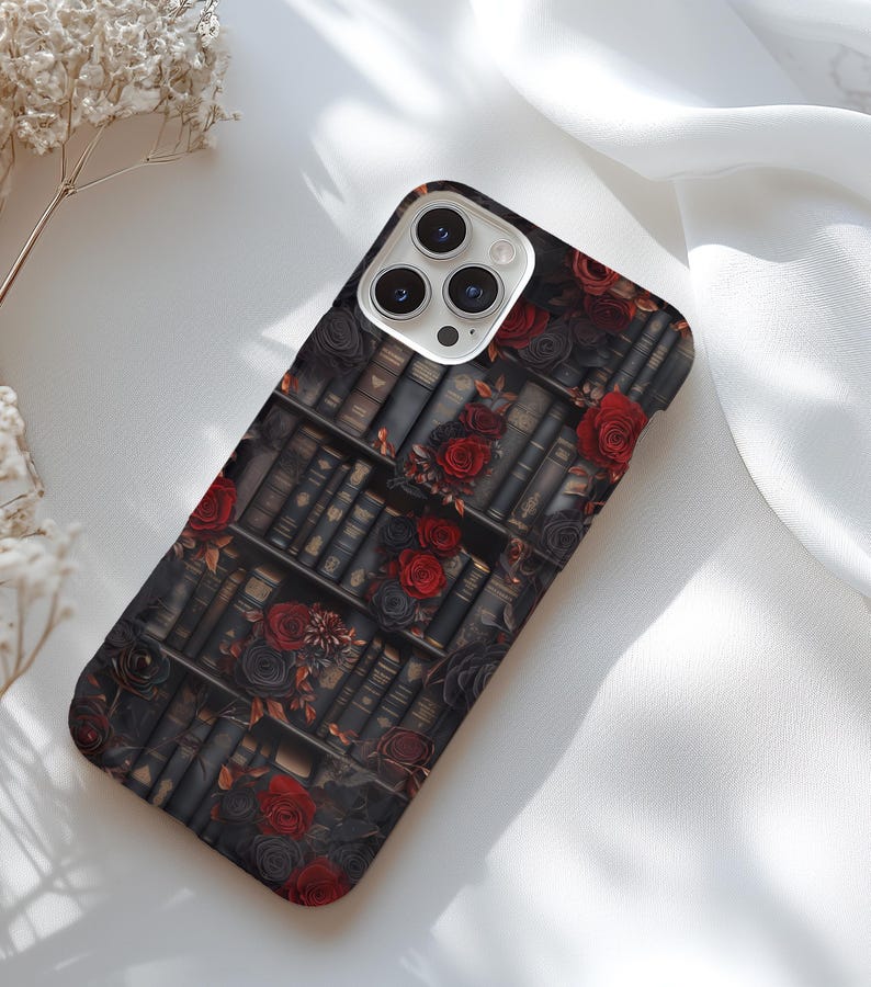 May include: A black phone case with a pattern of red roses and old books. The case has a camera lens cutout.