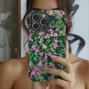 May include: A black phone case with a green and pink shamrock pattern. The case has a camera lens cutout.
