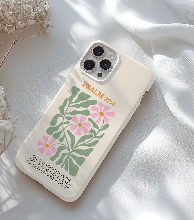 May include: A cream-colored phone case featuring a floral design with pink flowers and green leaves. The text "PSALM 37:4" is printed in orange, along with a quote. The case is designed to fit a smartphone and has a camera cutout.