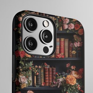Puede incluir: Una funda para tel&eacute;fono con un dise&ntilde;o de una estanter&iacute;a llena de libros y flores. La funda tiene un borde negro y un recorte para la c&aacute;mara.