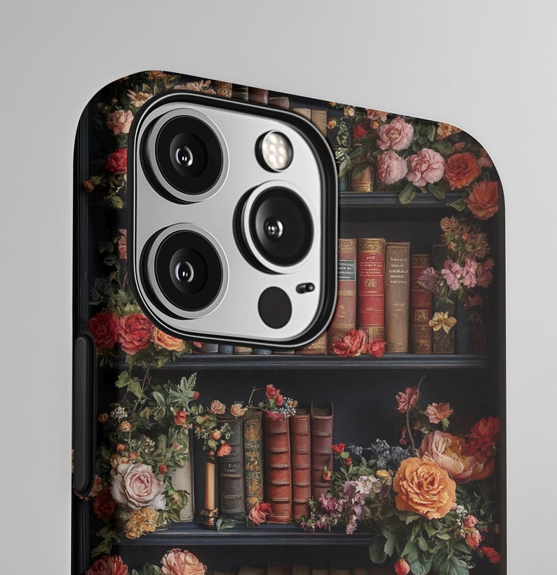 Puede incluir: Una funda para tel&eacute;fono con un dise&ntilde;o de una estanter&iacute;a llena de libros y flores. La funda tiene un borde negro y un recorte para la c&aacute;mara.
