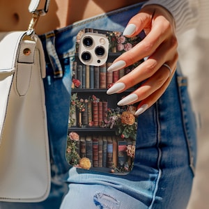Puede incluir: Una funda para tel&eacute;fono con un dise&ntilde;o floral y una estanter&iacute;a llena de libros. La funda tiene un recorte para el objetivo de la c&aacute;mara y un fondo blanco.