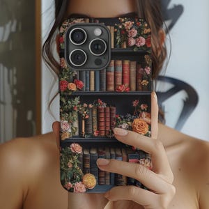 Puede incluir: Una funda de tel&eacute;fono negra con un dise&ntilde;o floral y una estanter&iacute;a llena de libros. La funda tiene una lente de c&aacute;mara con tres lentes.