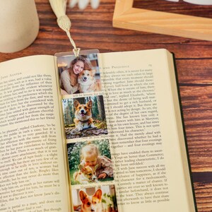 May include: A clear rectangular bookmark featuring four stacked photographic prints of a person and a corgi dog. The bookmark is topped with a cream-colored fabric tassel and is placed inside an open book with printed text on the pages.