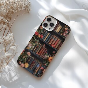 Puede incluir: Una funda de tel&eacute;fono negra con un dise&ntilde;o de una estanter&iacute;a llena de libros y flores. La lente de la c&aacute;mara es visible en la parte posterior de la funda.