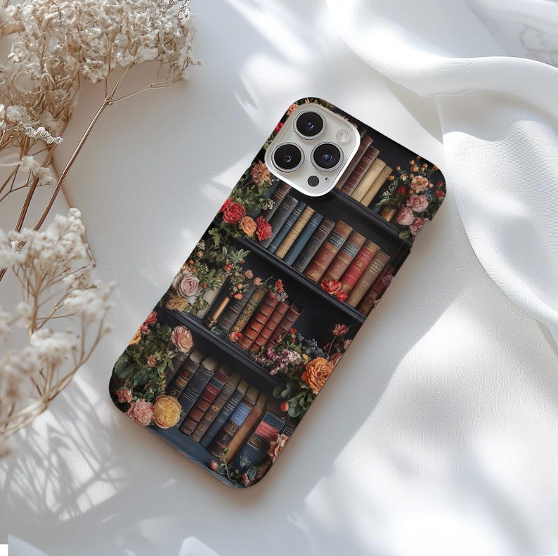 Puede incluir: Una funda de tel&eacute;fono negra con un dise&ntilde;o de una estanter&iacute;a llena de libros y flores. La lente de la c&aacute;mara es visible en la parte posterior de la funda.