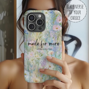 May include: A floral phone case with a watercolor design featuring pink, blue, and white flowers. The case has the text "made for more" and "Ephesians 2:10". The phone case is shown with a "Bible verse of your choice" option.