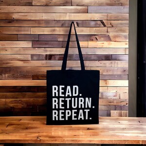 May include: Black tote bag with white text that reads "READ. RETURN. REPEAT."
