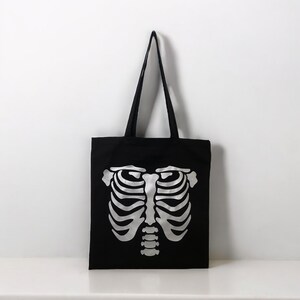 May include: Black canvas tote bag with a silver skeleton ribcage design.
