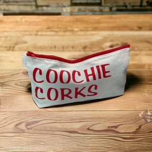 May include: A white canvas zippered pouch with a red zipper and the words "Coochie Corks" printed in red.