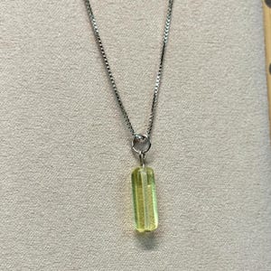 May include: A silver necklace with a rectangular, light green pendant. The pendant has vertical lines and a silver ring connecting it to the chain. The necklace is displayed against a neutral background.