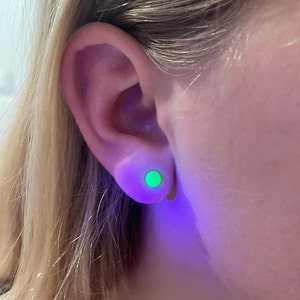 Könnte beinhalten: Ein Ohr mit einem grünen, im Dunkeln leuchtenden Ohrstecker. Der Ohrstecker ist eine kleine, runde Scheibe.