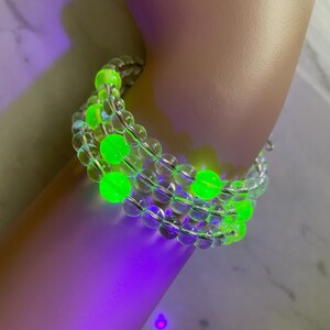 May include: A clear beaded bracelet with neon green accents. The bracelet is made of multiple strands of clear beads, with larger, round neon green beads interspersed throughout. The bracelet is wrapped around a wrist.