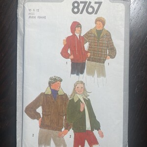 May include: A vintage Simplicity sewing pattern, number 8767, featuring illustrations of jackets and a hoodie. The pattern includes sizes 10 and 12, with the text "MISS JEUNE FEMME" at the bottom. The cover is white with a dark background.