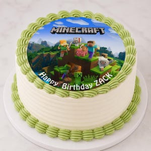 May include: A round cake with white frosting and green frosting trim. The top features a Minecraft-themed image with characters and the game's logo. The words "Happy Birthday Zack" are also on the cake.