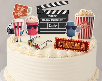 May include: A white frosted cake decorated with cinema-themed toppers. The toppers include popcorn, movie tickets, a clapperboard, 3D glasses, and a sign that says "CINEMA". The clapperboard says "Happy Birthday Emily".