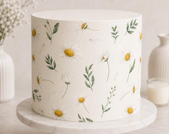 May include: A cylindrical cake with a smooth white finish, decorated with a repeating pattern of watercolor-style daisies featuring yellow centers and white petals, interspersed with delicate green leaves and thin stems.