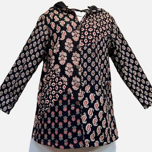 May include: A black hooded jacket with a button-up front and long sleeves. The jacket features a patchwork design with various patterns in red and white on a black background. The jacket has two pockets and wooden buttons.