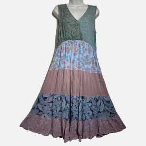 May include: A sleeveless tiered dress featuring a V-neckline and a patchwork design. The bodice combines olive green floral and light green patterns, while the skirt sections display light blue floral, solid mauve, and dark blue leaf prints.
