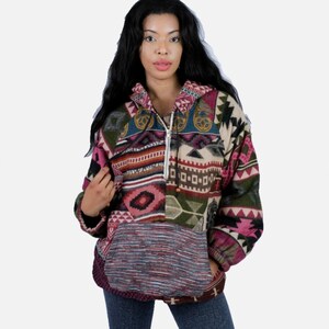 May include: A long-sleeve hooded pullover featuring a quarter-zip neckline and a large front kangaroo pocket. The garment displays a multi-colored patchwork pattern with geometric shapes in shades of pink, green, blue, and cream, with a textured grey pocket.