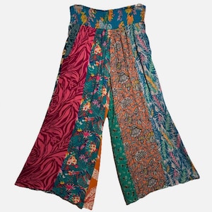 May include: Wide-leg pants with a patchwork design. The pants feature panels of various patterns, including floral, abstract, and leaf prints in shades of pink, teal, orange, and blue. The waistband is elasticized.