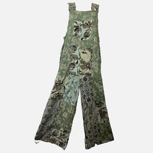 May include: A sage green jumpsuit featuring a patchwork design with various floral and botanical patterns. The garment has wide legs, a square neckline, and thick shoulder straps. The fabric displays a mix of light and dark green tones.