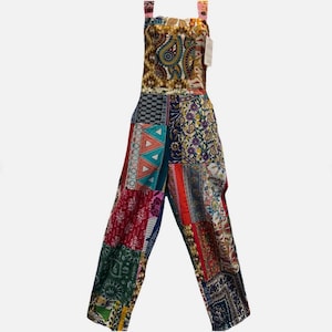 May include: A patchwork jumpsuit with a variety of colorful patterns. The top features a paisley design, while the legs showcase a mix of geometric and floral prints in shades of red, blue, green, and purple. The jumpsuit has adjustable straps.