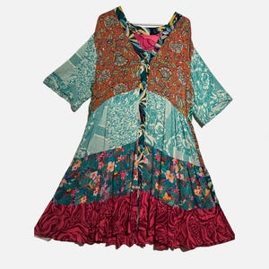 May include: A patchwork dress with a V-neckline and short sleeves. The dress features a variety of floral and patterned fabrics in shades of teal, orange, pink, and burgundy. The dress has a tiered skirt and a relaxed fit.