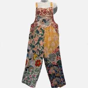 May include: A colorful floral print jumpsuit with adjustable straps. The jumpsuit features a patchwork design with various floral patterns in shades of red, yellow, green, and blue. The garment is displayed on a white mannequin.