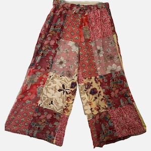May include: Wide-leg pants featuring a patchwork design with various floral and paisley patterns in shades of red, pink, cream, and burgundy. The garment has an elasticized waistband with a drawstring tie and a loose, flowing silhouette.