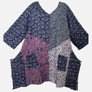 May include: A long-sleeved tunic featuring a V-neckline and a button-down front. The garment is constructed from a patchwork of various floral-patterned fabrics in shades of navy blue, light purple, white, and pink, including two front pockets.