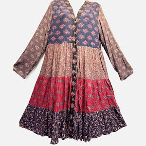 May include: A long-sleeved tiered dress featuring a button-down front and a V-neckline. The garment displays a patchwork design with horizontal sections in navy blue, muted mauve, bright pink, and dark blue, all adorned with floral patterns.
